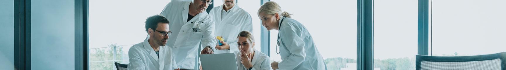 A group of scientists in lab codes gathered around a laptop in a conference room