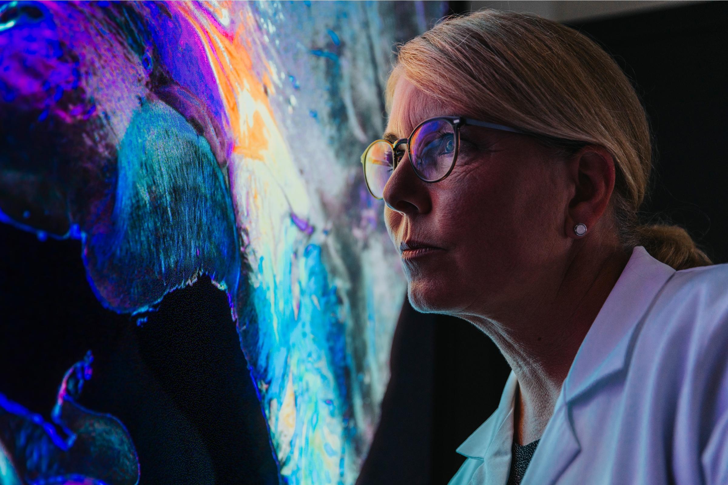 Female researcher looking as a large screen displaying a visualization of brain fibers